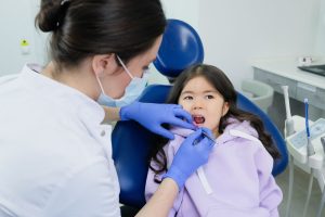 Niña en el sillón dental con la boca abierta mientras una odontóloga con guantes azules revisa su paladar con un espejo